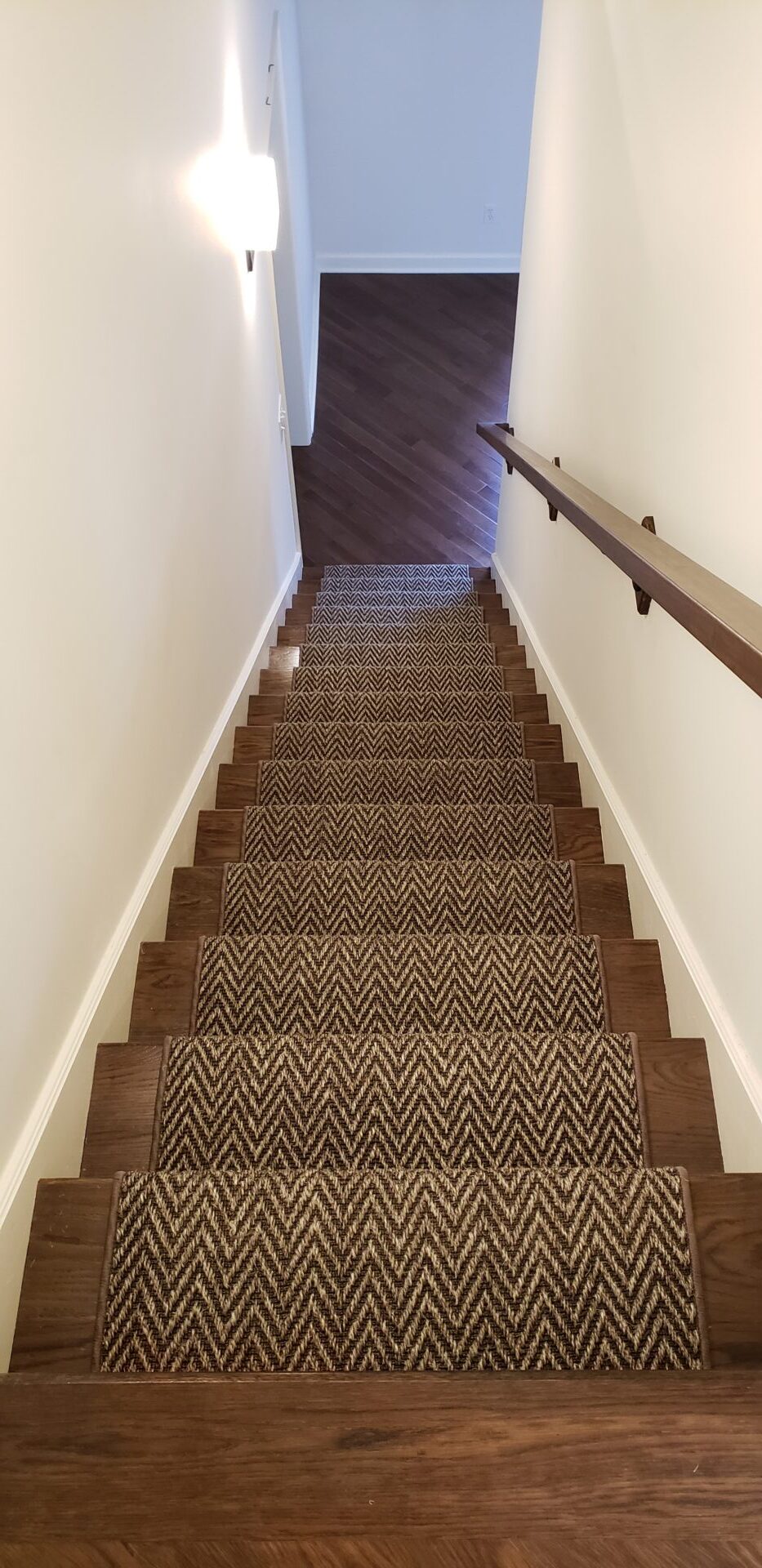 A staircase with brown carpet and wooden handrail.