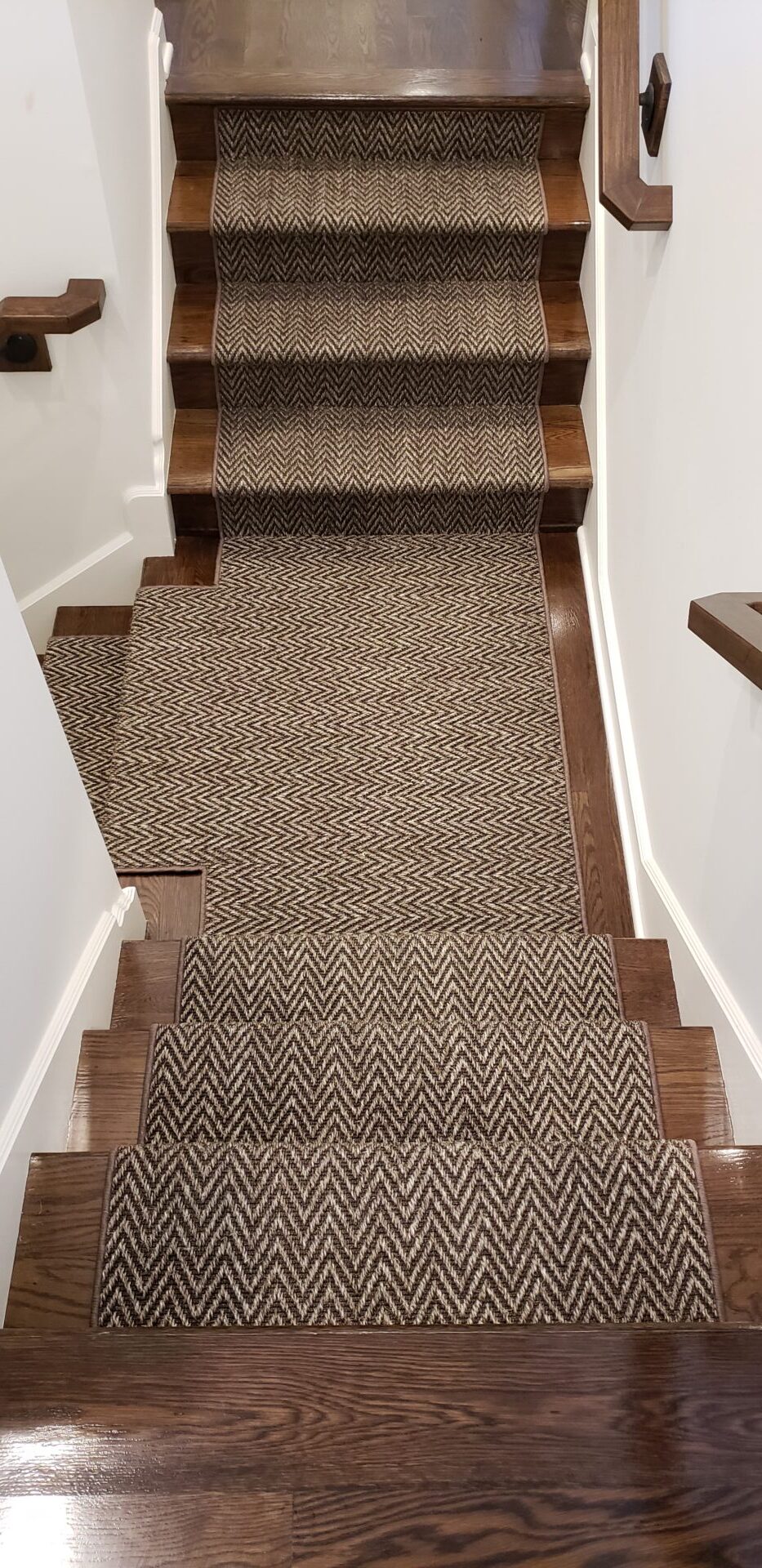 A carpet stair runner with wood trim on the bottom.