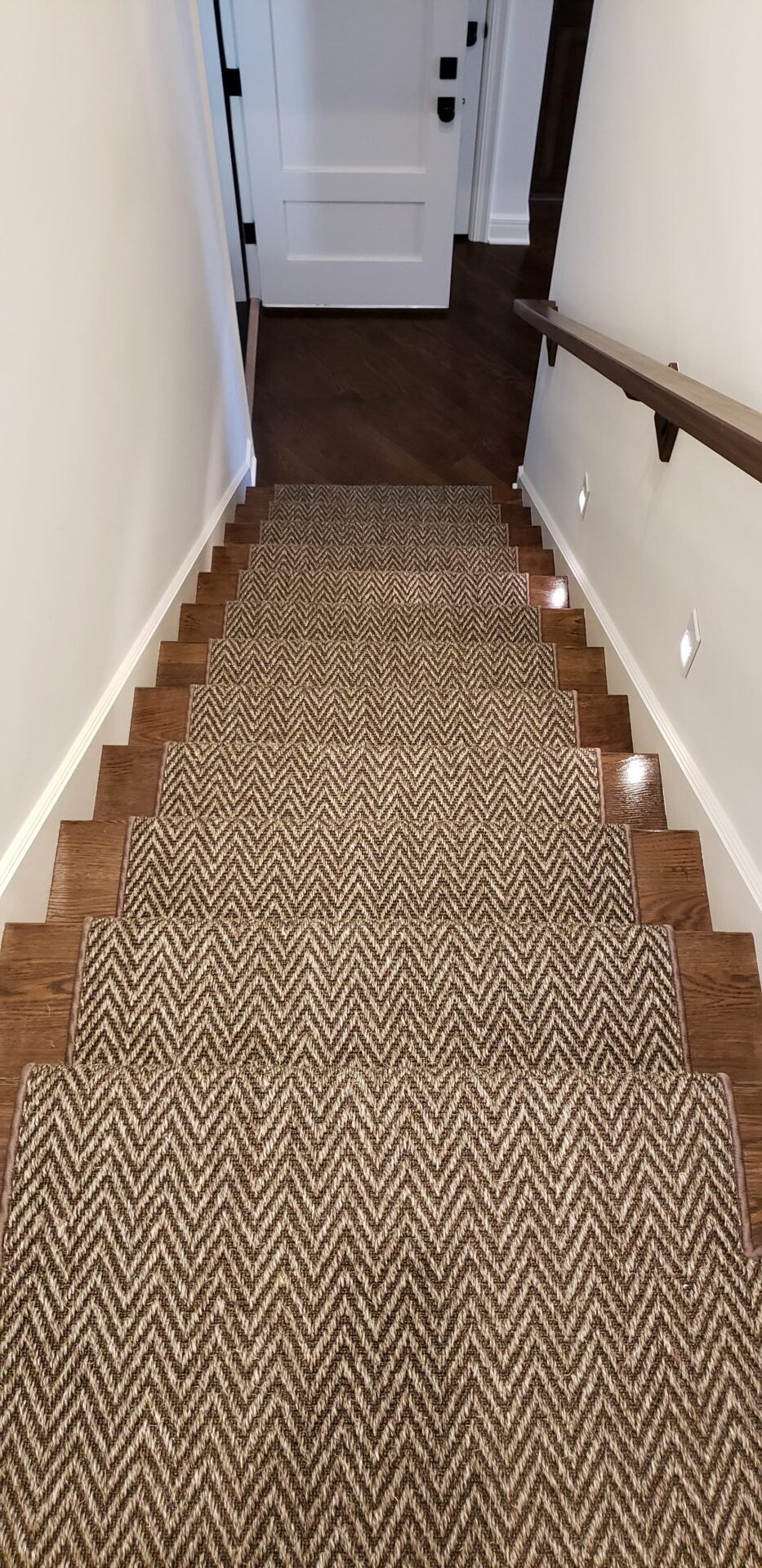 A carpet on the bottom of stairs with wood floors.